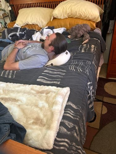 A young man with a beard lying on a bed with Hizoo under his neck