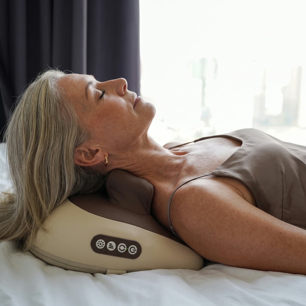 Woman in her late 50s lying in bed with the HiZoo neck massager under her neck